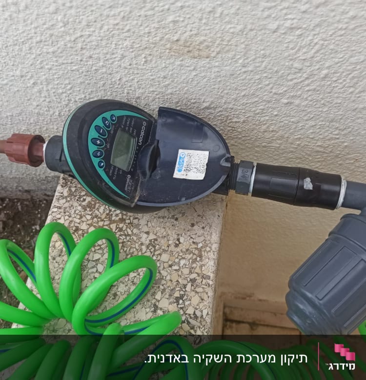 טיימר השקיה מחובר לצינור ירוק בגינה